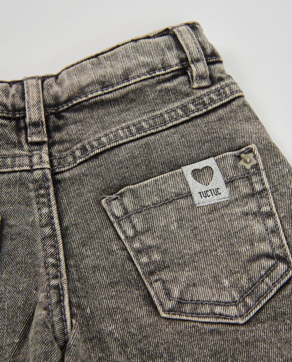 Pantolonun arka cebi yakın planda; kalp logolu TUCTUC etiketi ve ağartmalı denim dokusu görünüyor.