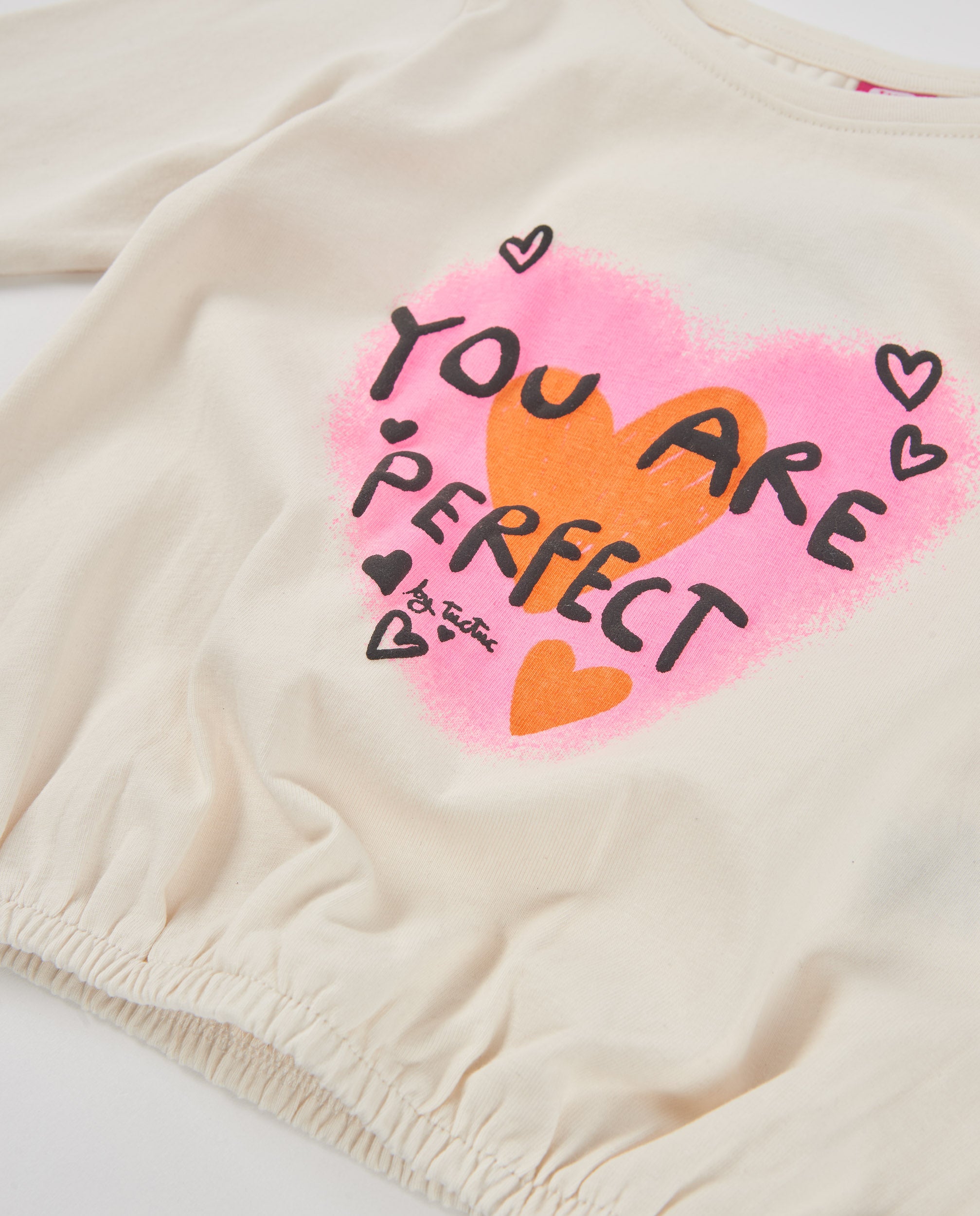 Tişörtün göğsündeki You Are Perfect kalp baskısı ve lastikli etek ucu yakın planda görünüyor.