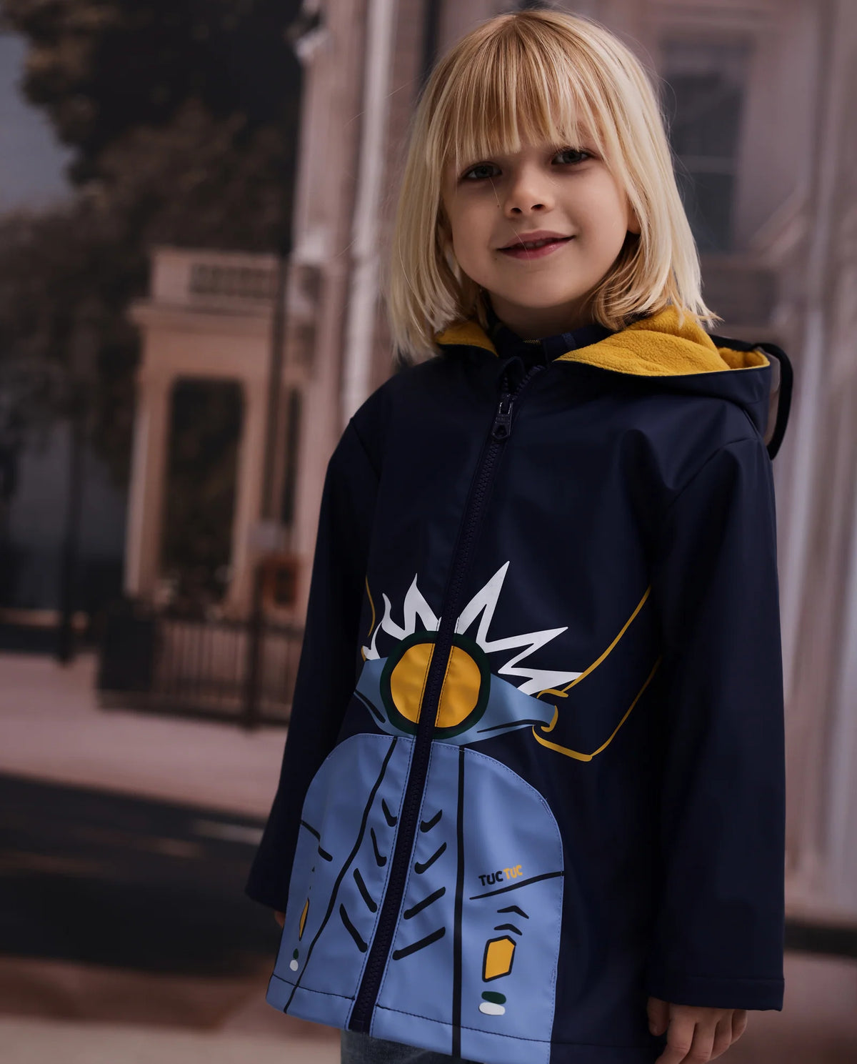 Tuc Tuc lacivert vespa figürlü yağmurluk erkek çocuk üzerinde; sarı polar astarlı kapüşon ve baskı görünüyor.