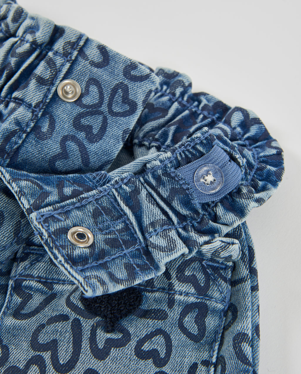 Kot pantolonun büzgülü bel bandı, çıtçıt ve düğme detayları kalpli denim üzerinde yakın planda.