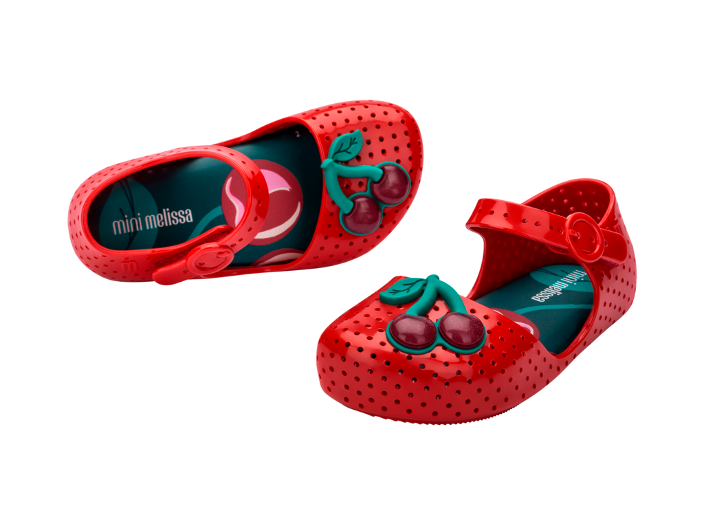 Mini Melissa Furadinha Cherry BB kırmızı kirazlı çocuk ayakkabısı – çapraz görünüm, tatlı kiraz aplikeleriyle sevimli ve konforlu stil