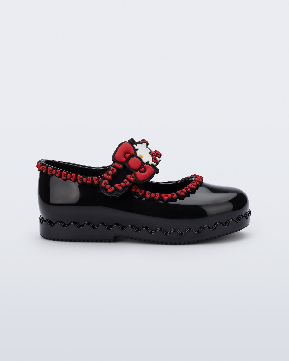 Mini Melissa Hip Ballerina siyah babet, Hello Kitty rozeti ve kırmızı fiyonk detayıyla yan açıdan görünüyor.
