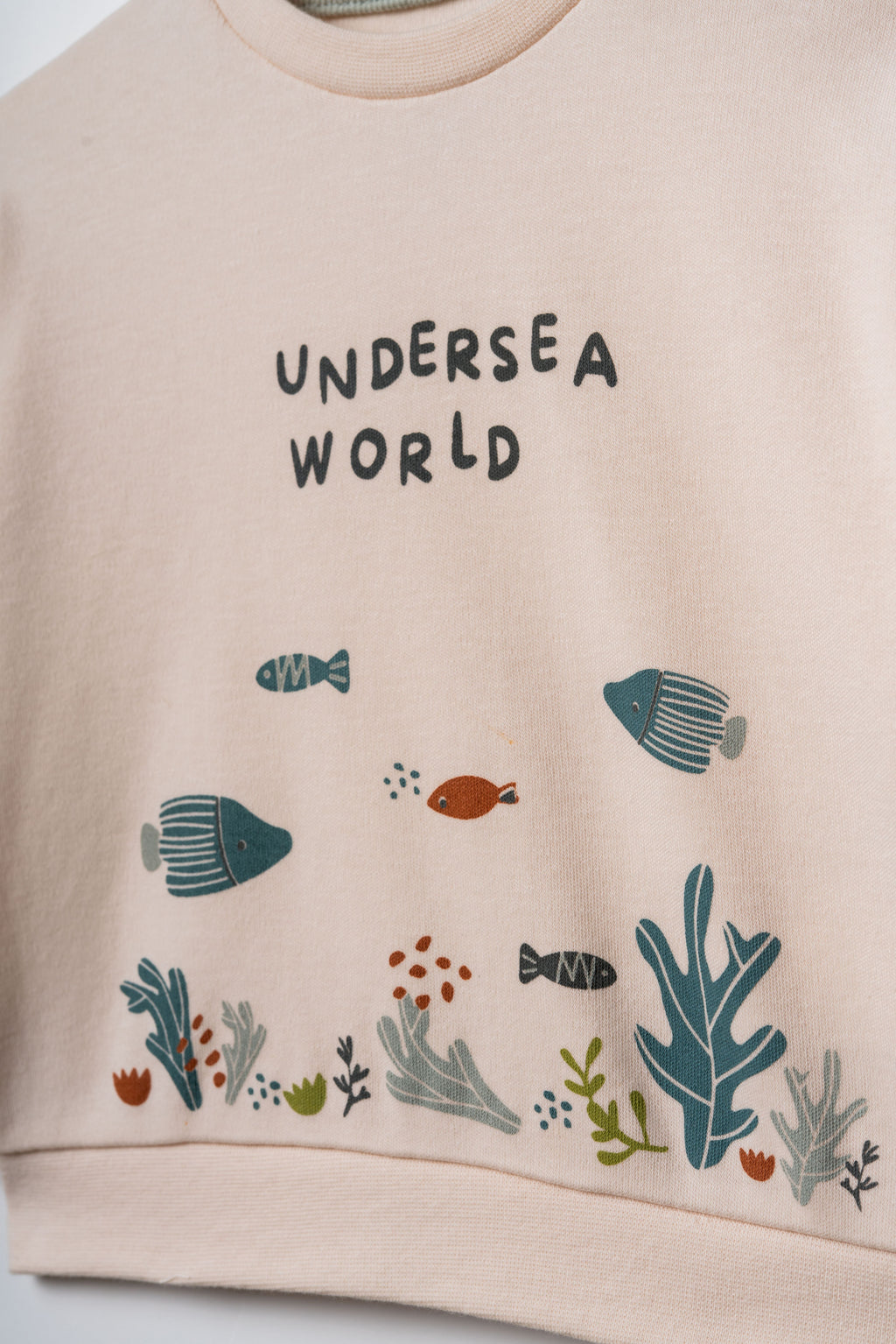 Pudra peach organik pamuk bebek sweatshirtü, göğüsteki Undersea World yazısı ve deniz altı illüstrasyonu yakın çekim