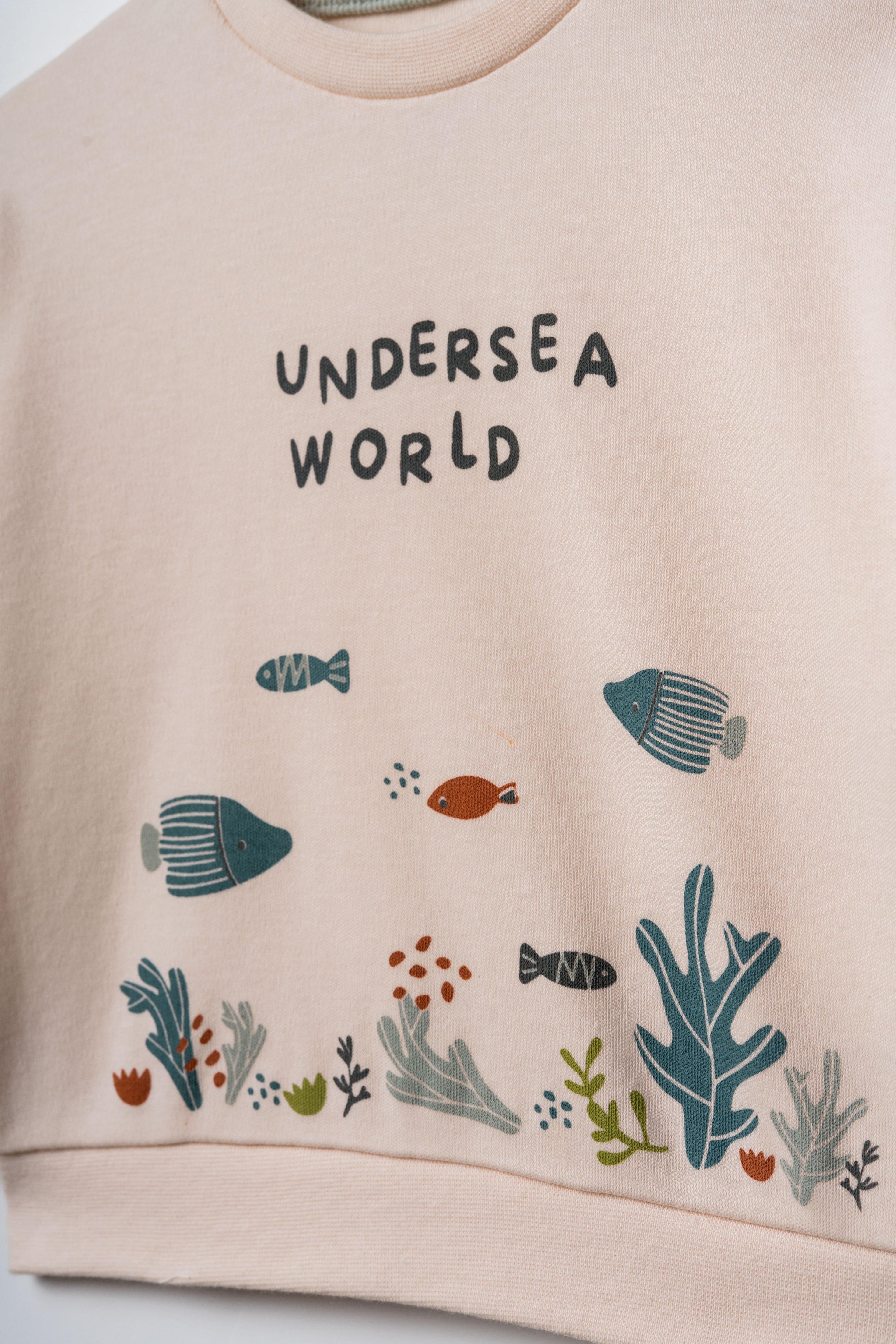 Pudra peach organik pamuk bebek sweatshirtü, göğüsteki Undersea World yazısı ve deniz altı illüstrasyonu yakın çekim