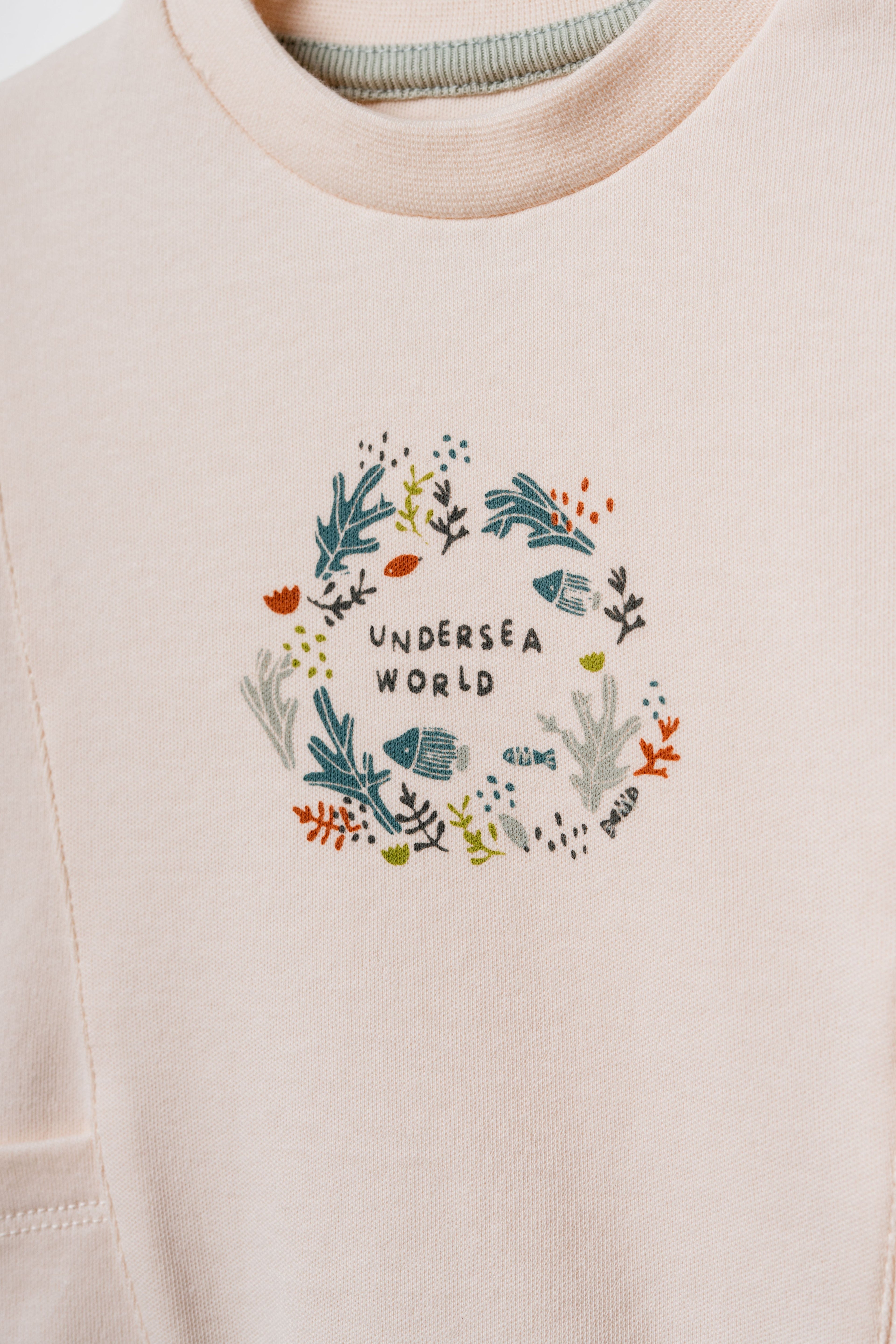 Pudra peach organik pamuk bebek sweatshirtü, göğüsteki Undersea World çelenk baskısı ve deniz altı illüstrasyonu yakın çekim
