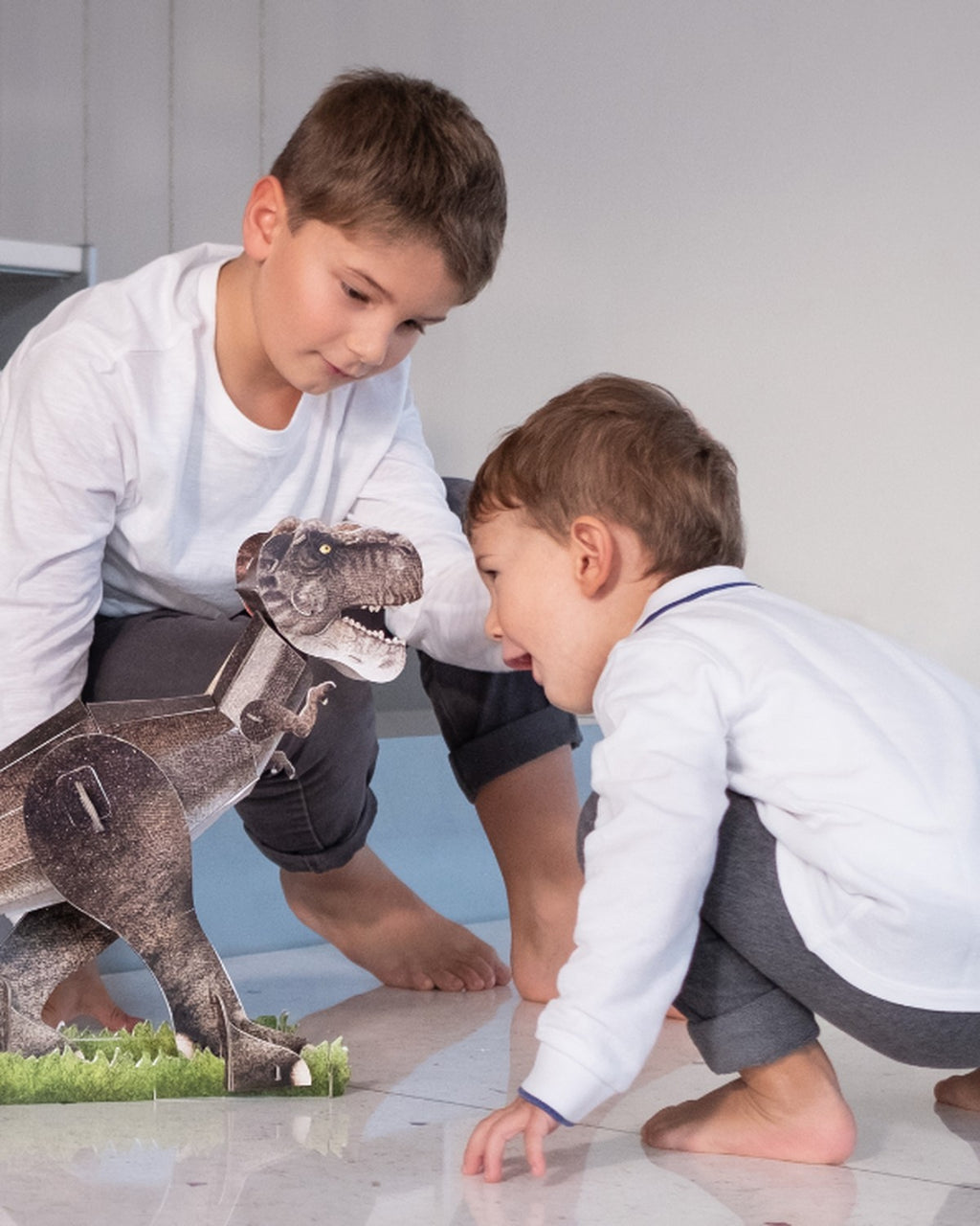 İki erkek çocuk yerde kurulmuş T-Rex modeliyle oynuyor