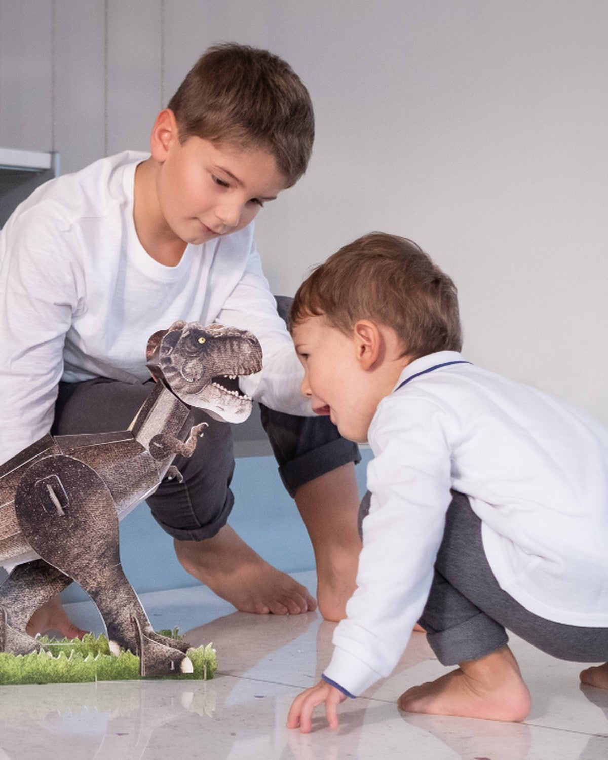 İki erkek çocuk yerde kurulmuş T-Rex modeliyle oynuyor