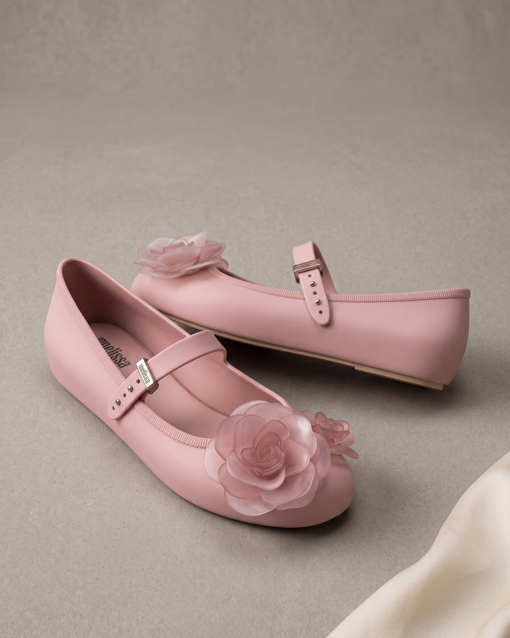 Arkadan gelen ışıkla içeriden aydınlanan şeffaf gül aplike; Melissa Soft Ballerina Petals pembe babetin organze dokusu yakın planda.