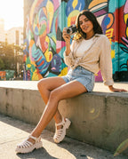 Vintage kot şort ve keten gömlek kombini ile şehirde oturan bir mankenin ayağındaki bej Melissa Possession Platform II platform sandaletler; güneşli ve renkli bir dış mekanda genel plan yaşam tarzı fotoğrafı.