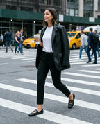 Siyah deri blazer ve kısa paça pantolon kombini ile şehirde yürüyen bir kadının ayağındaki siyah Melissa Soft Ballerina Studs zımbalı babetler; genel plan dinamik sokak stili fotoğrafı.