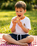 Miela Kids pizza takımı giyen erkek çocuk piknik örtüsünde pizza dilimiyle oturuyor