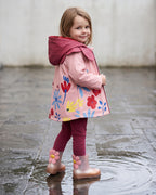 Mini Melissa kız çocuk yağmur çizmesi giyen çocuk; pembe-bakır ombre çizme, çiçek aplike, pembe yağmurluk ve bordo tayt kombini.