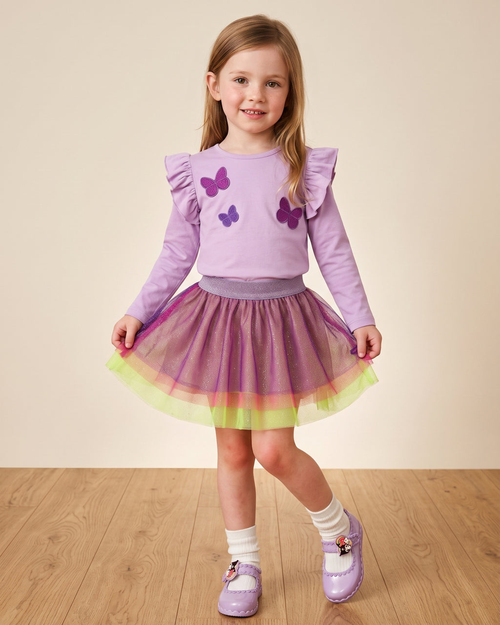 Mini Melissa Kuromi ayakkabı giyen kız çocuk; sedefli lila babet, tüllü simli etek ve kelebek aplikeli lila tişört kombini.
