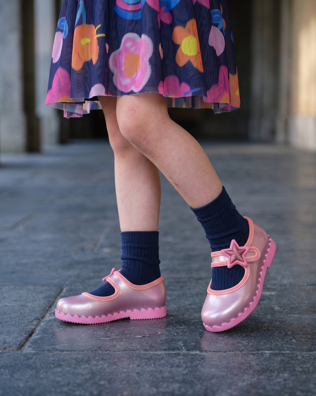 Mini Melissa pembe abiye ayakkabı detayı: sedefli metalik babet, üç sıra biye, simli yıldız rozet ve lacivert çorap.