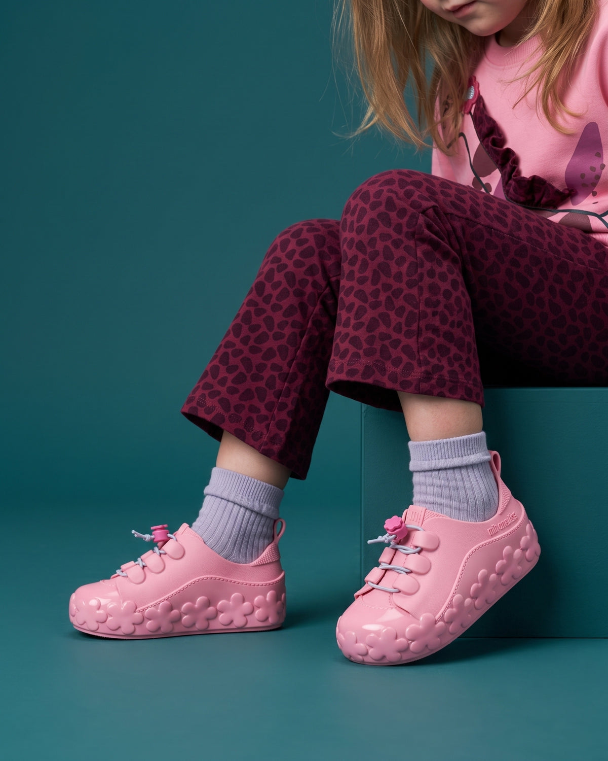Mini Melissa pembe sneaker detayı: çiçek kabartmalı taban, fuşya çiçek stoperli lastik bağcık ve lavanta çorap.