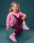 Mini Melissa pembe spor ayakkabı giyen kız çocuk; çiçek tabanlı sneaker, zürafa baskılı pembe sweatshirt ve bordo ispanyol paça takım.