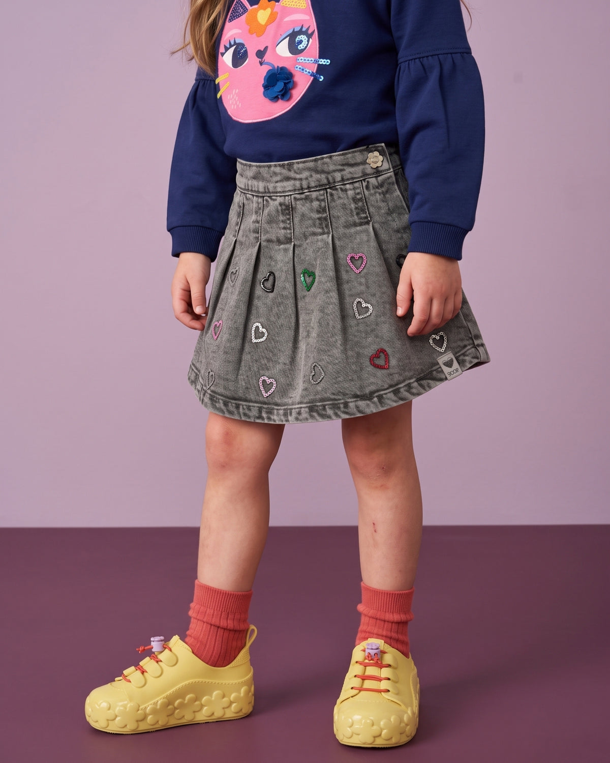 Mini Melissa sarı spor ayakkabı detayı: çiçek kabartmalı taban, lila çiçek stoperli kırmızı lastik bağcık ve mercan çorap.