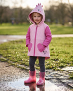 Mini Melissa simli ayakkabı giyen kız çocuk; şeffaf pembe yağmur çizmesi, gümüş kalp simler ve pembe dinozor yağmurluk kombini.