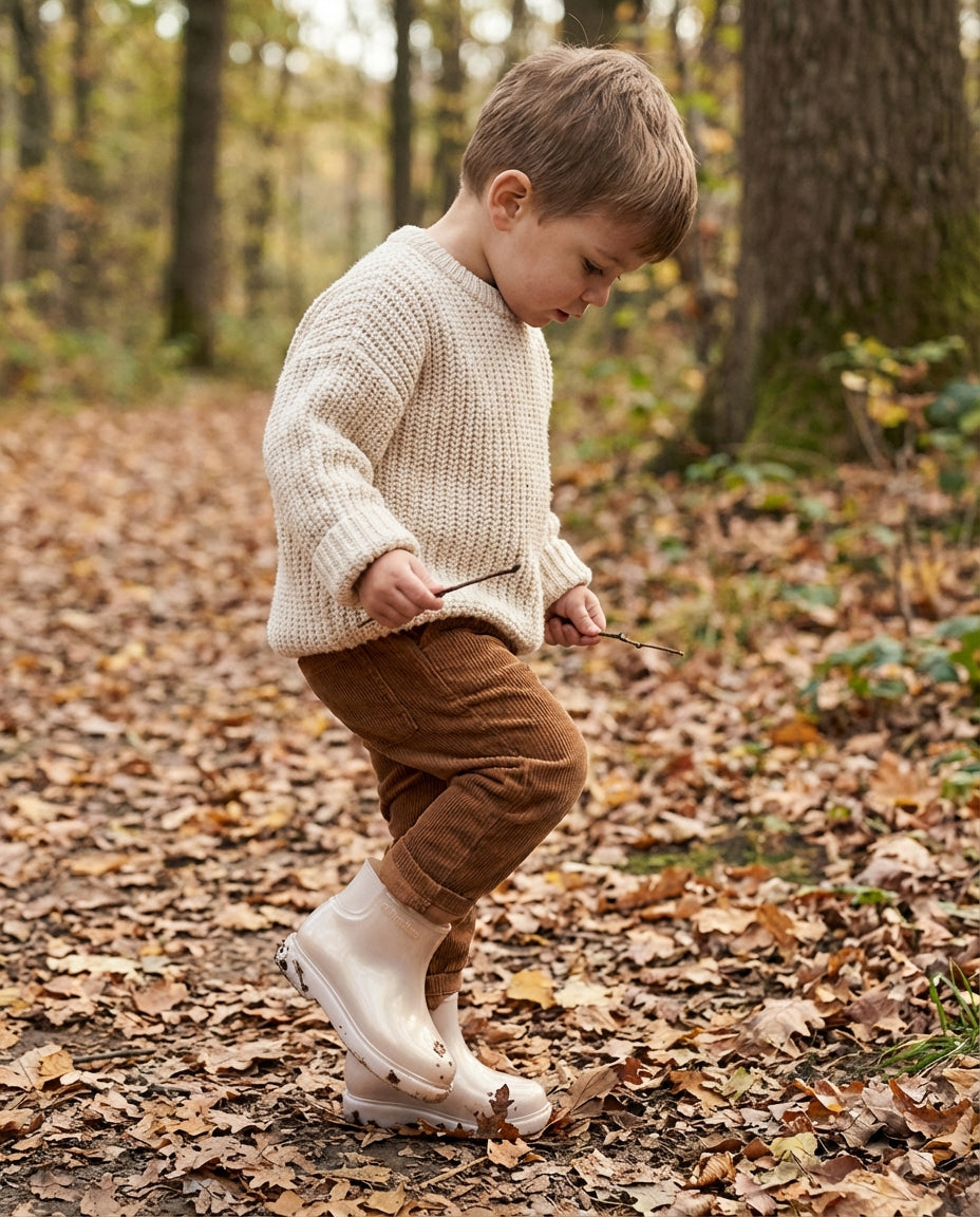 Toprak tonlarında kombinle sonbahar yaprakları üzerinde yürüyen 3 yaşındaki çocuğun ayağında orantılı Mini Melissa bej Chelsea bot