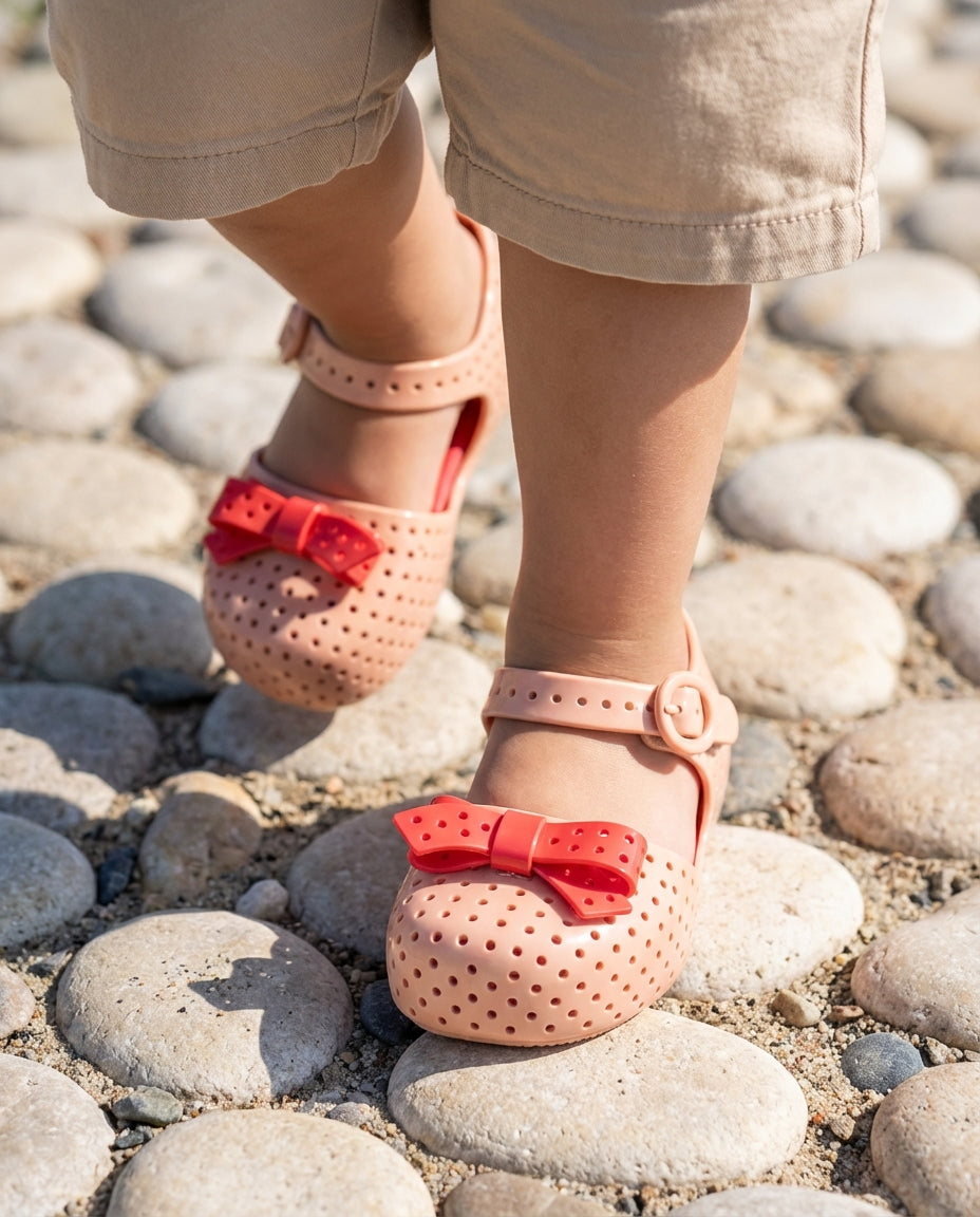 Bej şortla adım atan 2 yaşındaki miniğin ayağını saran çıt çıt bantlı Mini Melissa delikli yazlık ayakkabı yakın plan
