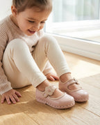 Ahşap zeminde oturup pembe çiçekli Mini Melissa babetlerine hayranlıkla bakan kız çocuğu