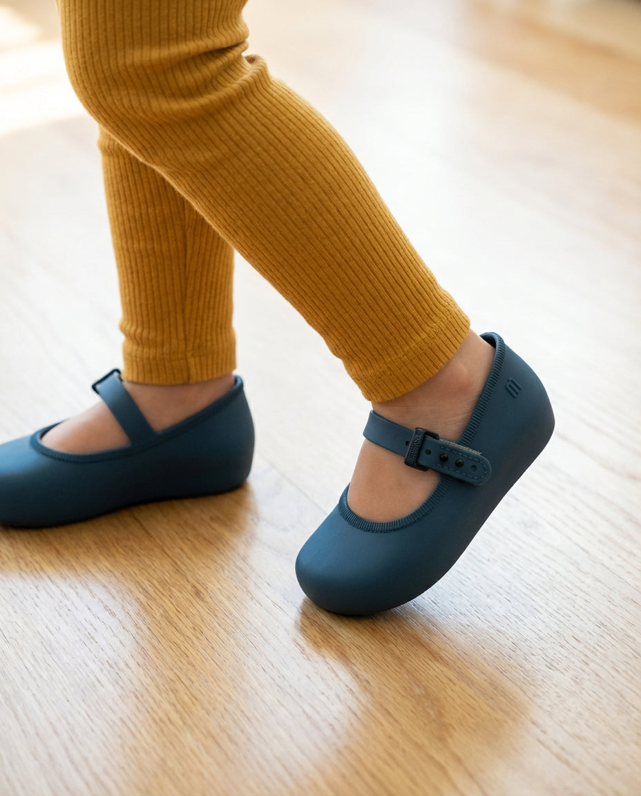 Hardal sarısı taytla adım atan 2 yaşındaki miniğin ayağını güvenle saran pratik Mini Melissa koyu mavi babet yakın plan