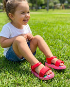 Çimlerde oynayan 2 yaşındaki kız çocuğunun ayağında renkli desenli pembe Mini Melissa yazlık sandalet
