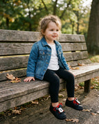 Kot ceket ve siyah tayt kombiniyle parkta oturan 3 yaşındaki kız çocuğunun ayağında rahat Mini Melissa siyah sneaker