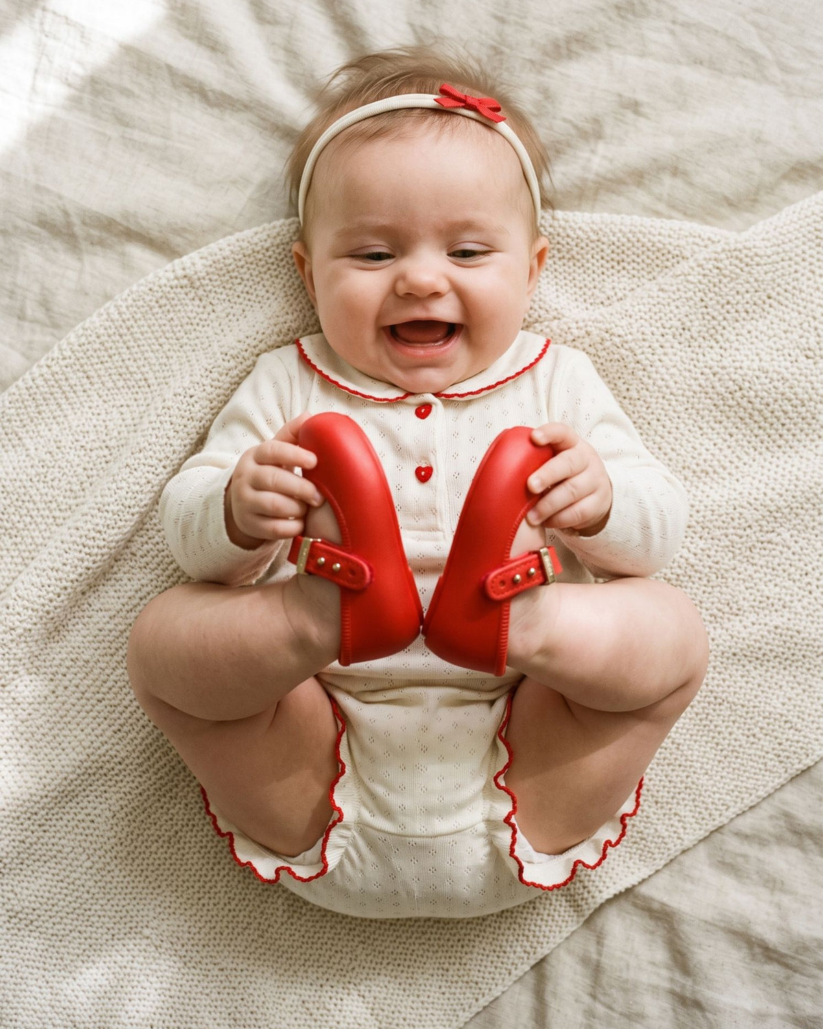 Kırmızı Mini Melissa My First Ballerina babetli ayaklarını elleriyle tutup gülen kız bebek