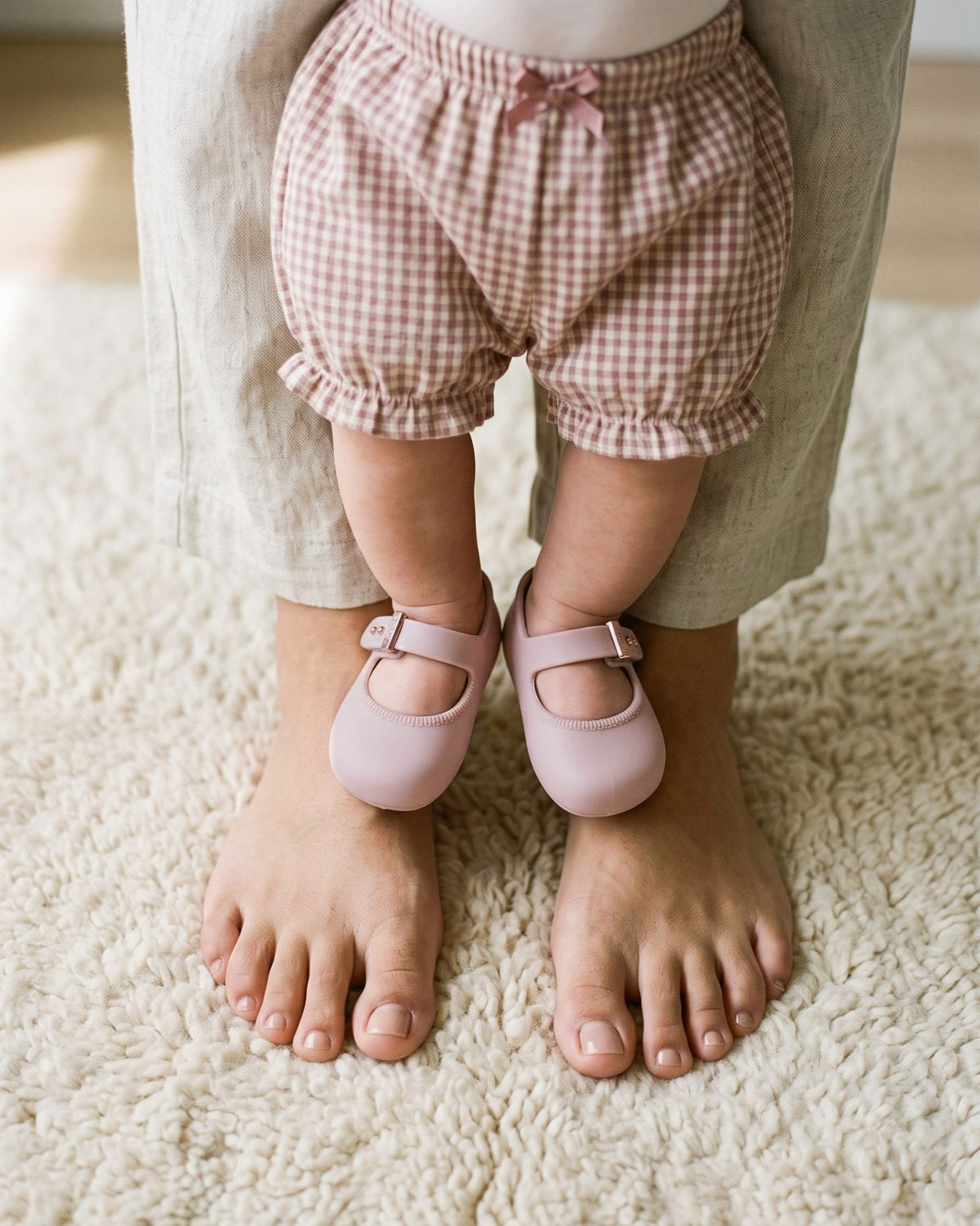 Annesinin çıplak ayaklarının üstünde duran, pudra pembe Mini Melissa My First Ballerina giymiş kız bebek