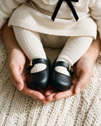 Annesinin avucunda siyah Mini Melissa My First Ballerina ve fildişi çorap giymiş bebek ayakları, 17 numara yenidoğan babeti