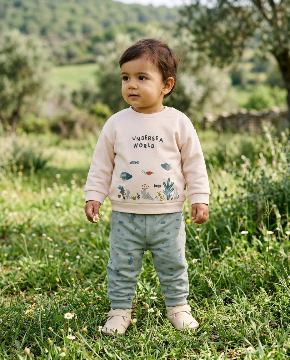 Bahar kırında ayakta duran Türk bebeği, organik pamuk Undersea World sweatshirt ve mint yeşili eşofman giymiş