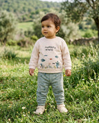 Bahar kırında ayakta duran Türk bebeği, organik pamuk Undersea World sweatshirt ve mint yeşili eşofman giymiş