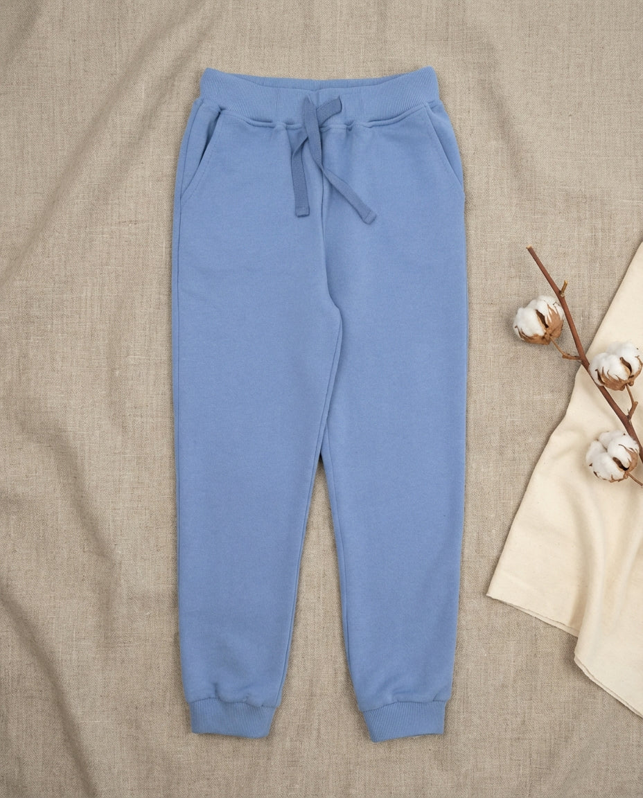 GOTS organik pamuk cornflower blue çocuk jogger pantolon linen zemin düz çekim, pamuk çiçeği prop detayı