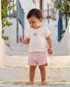 Ege sokağında taş merdivende oturan Türk bebeği, organik pamuk Little Princess yazılı ekru ve pembe pointel takım giymiş