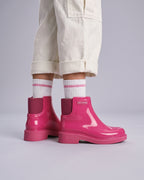 Okul çağındaki kız çocuğunun ayağında parlak Mini Melissa pembe bot; pembe çizgili beyaz çorap, kalın mat taban ve bir ton koyu böğürtlen renkli elastik yan körük yakın planda.
