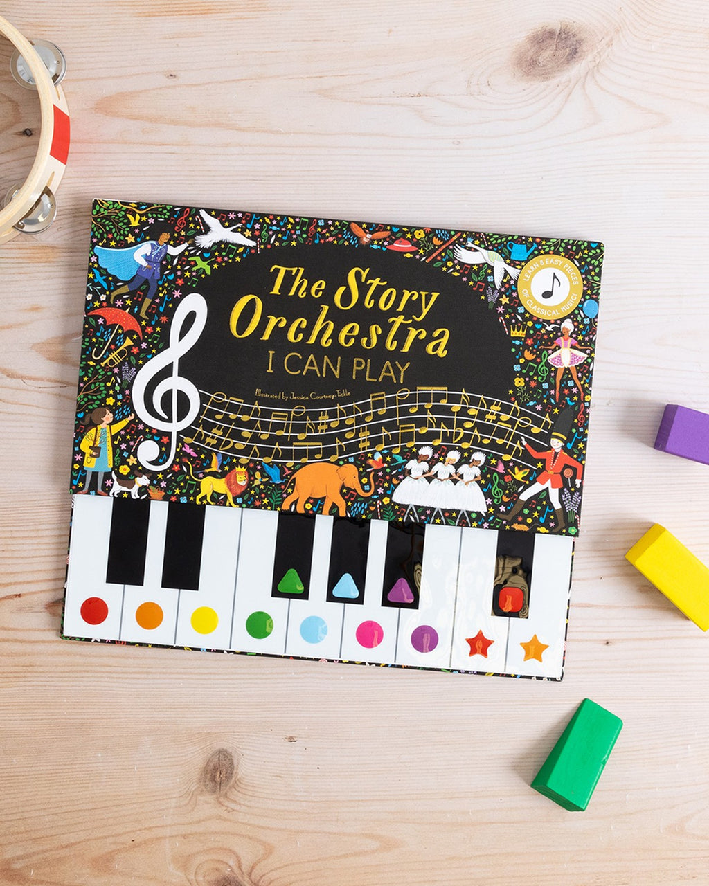 Ahşap masa üzerinde The Story Orchestra I Can Play kitabı, yanında renkli oyuncak bloklar
