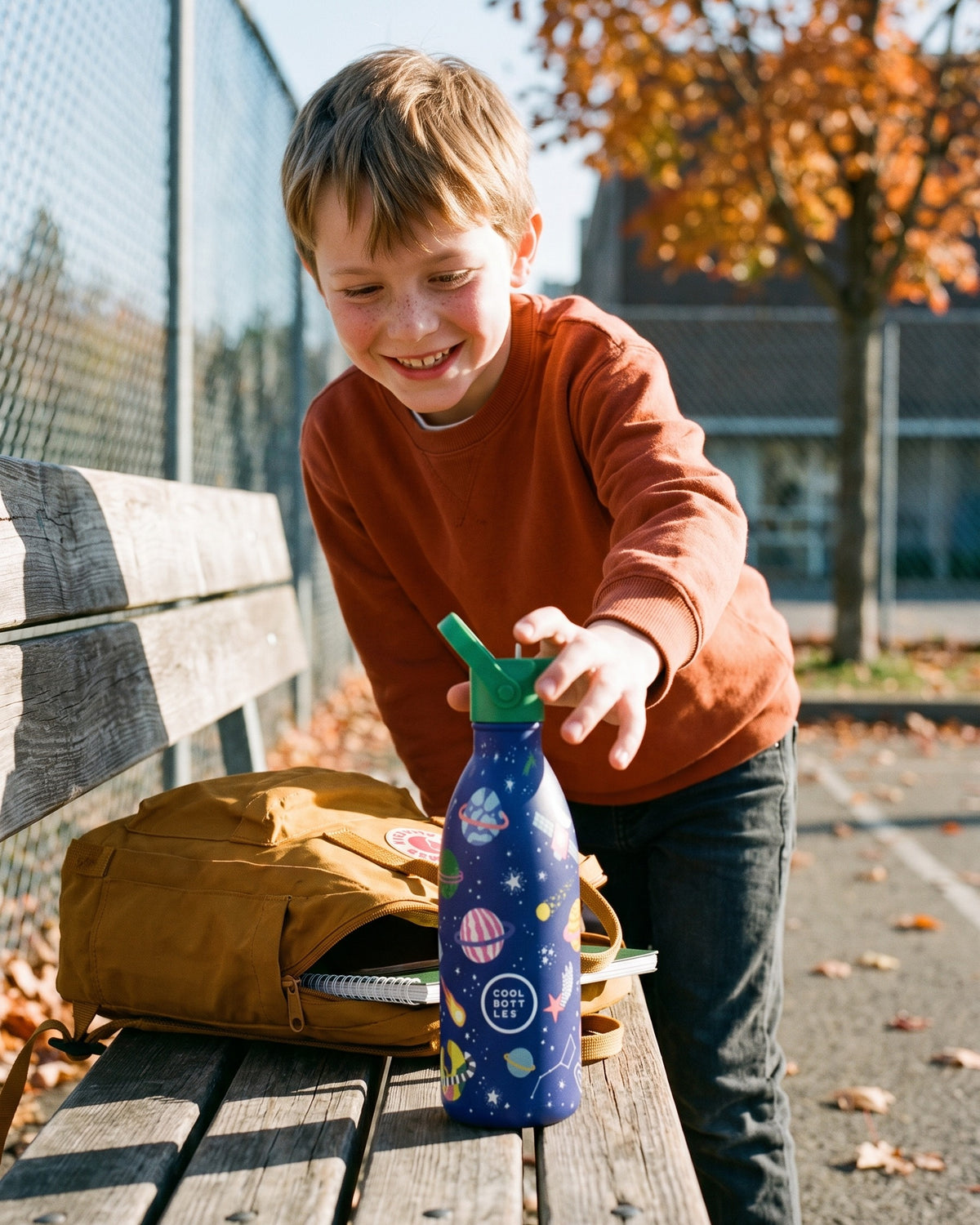 Cool Bottles Kids uzay desenli çelik matara, okul bahçesi bankında