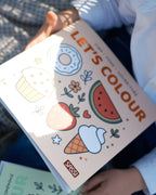 Çocuğun kucağında duran Let's Colour Food boyama kitabının kapağı